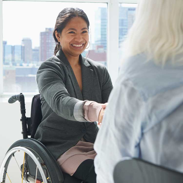 Mujer en silla de ruedas sonriendo saluda a otra persona