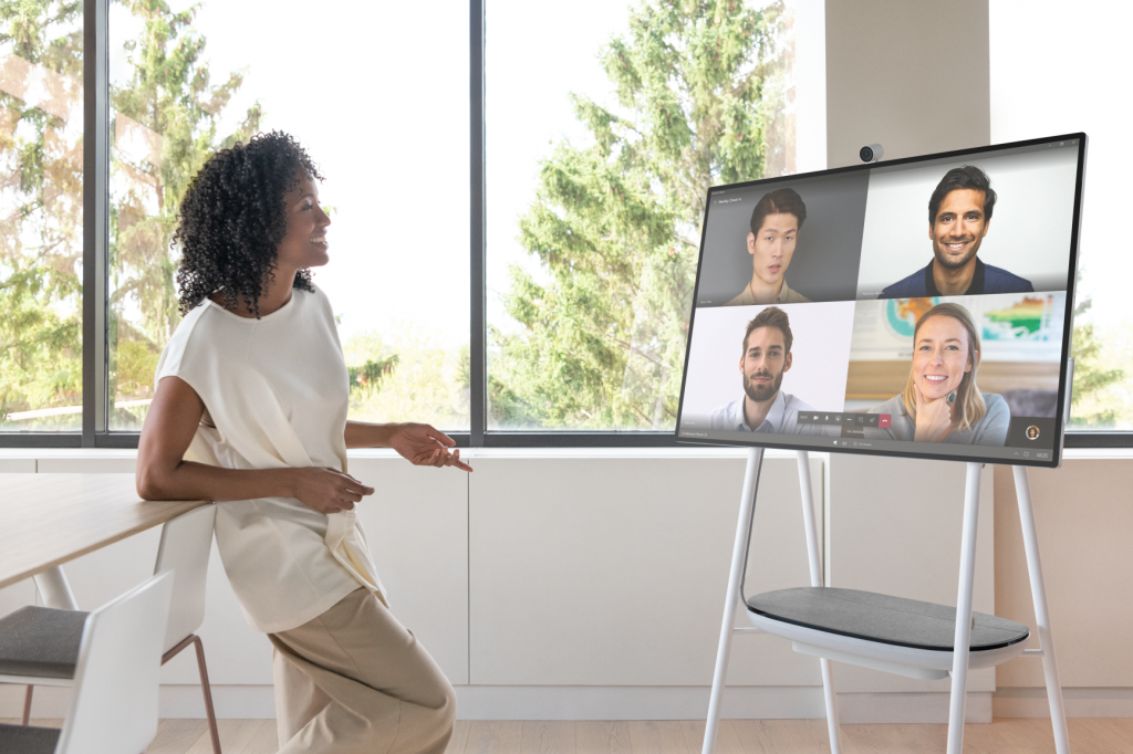 A woman presents remotely to 4 people on a Surface Hub.