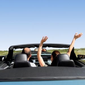 Two people in a blue convertible with their hands up in the air